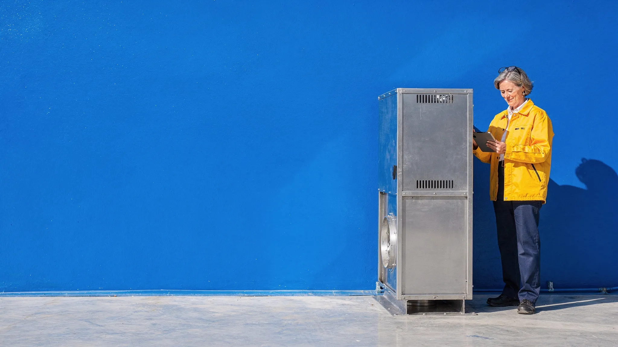 Une responsable de production vérifie une unité de filtration d'air, tablette en main, devant un mur bleu